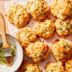 Cheddar bay biscuits on a surface with butter topping on the side.