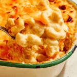 A scoop of baked mac and cheese being lifted out of a baking dish.