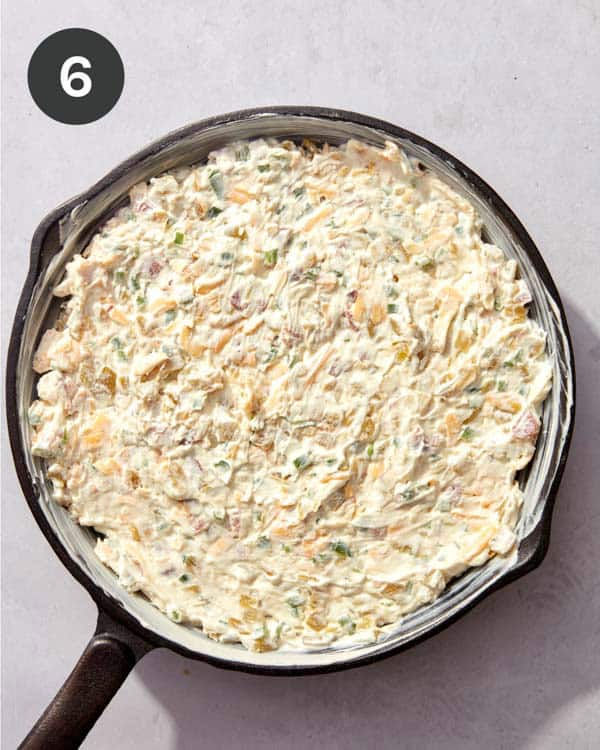 A cast iron skillet filled with Jalapeño popper dip ready to go into the oven.