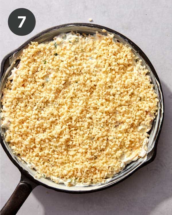 Jalapeño popper dip topping mixture spread over the dip in a cast iron skillet.