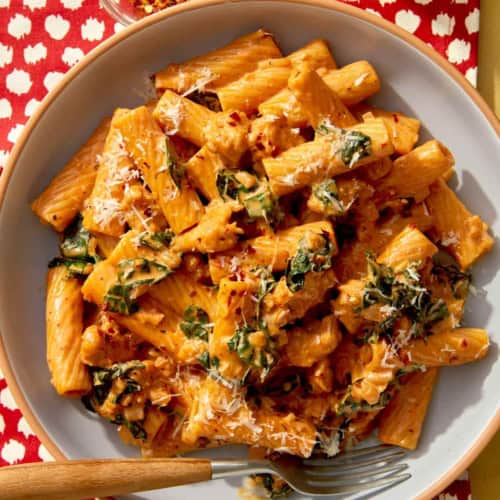 Close up on a bowl of kale and sausage rigatoni in a bowl with a fork.