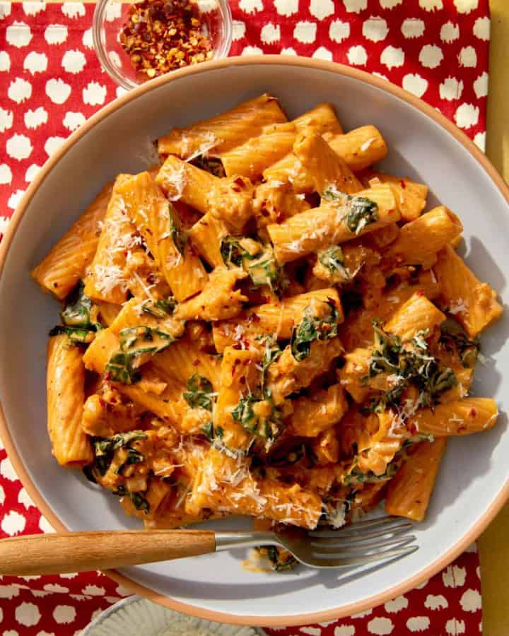 Close up on a bowl of kale and sausage rigatoni in a bowl with a fork.