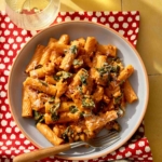 Kale and sausage rigatoni pasta in a bowl with wine on the side.