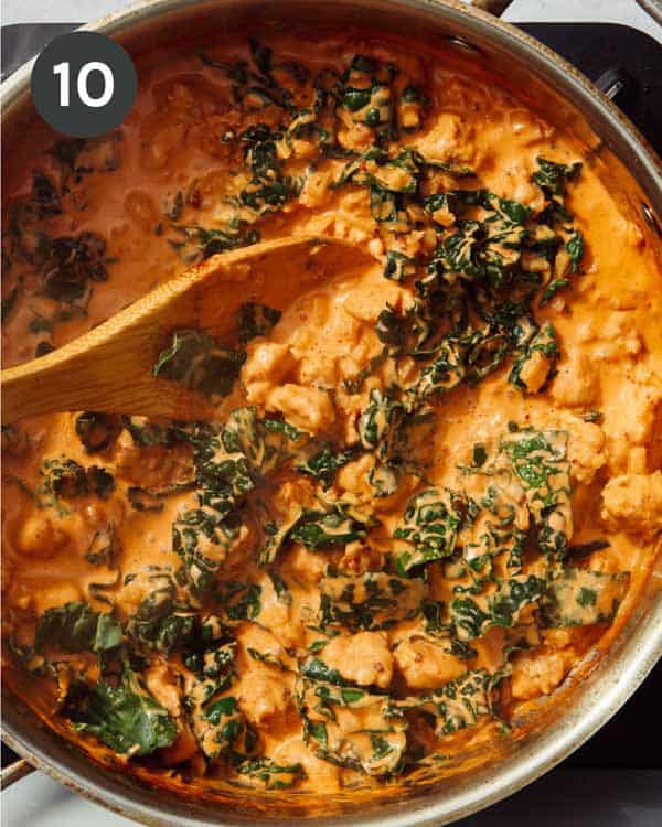 Rigatoni pasta tossed with sausage and kale and a red sauce in a skillet.