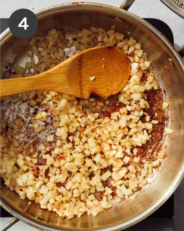 A skillet cooking some chopped fennel with a wooden spoon.
