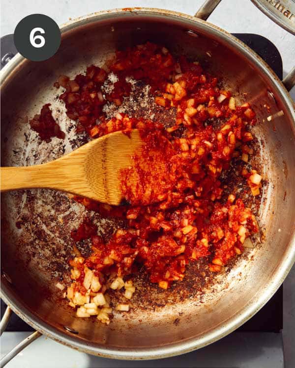 Tomato paste with some chopped vegetables in a skillet cooking.