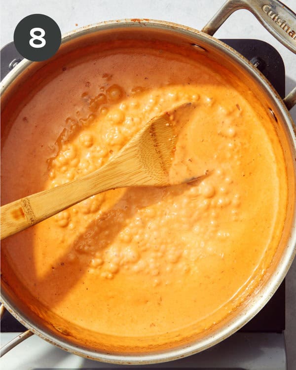 A red sauce pasta sauce simmering in a skillet with a wooden spoon.