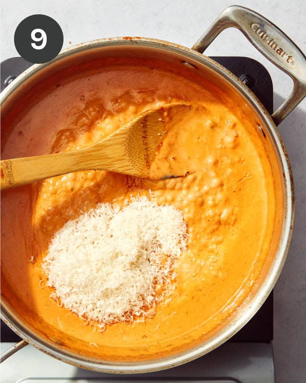 A red sauce pasta with parmesan being added to the skillet.