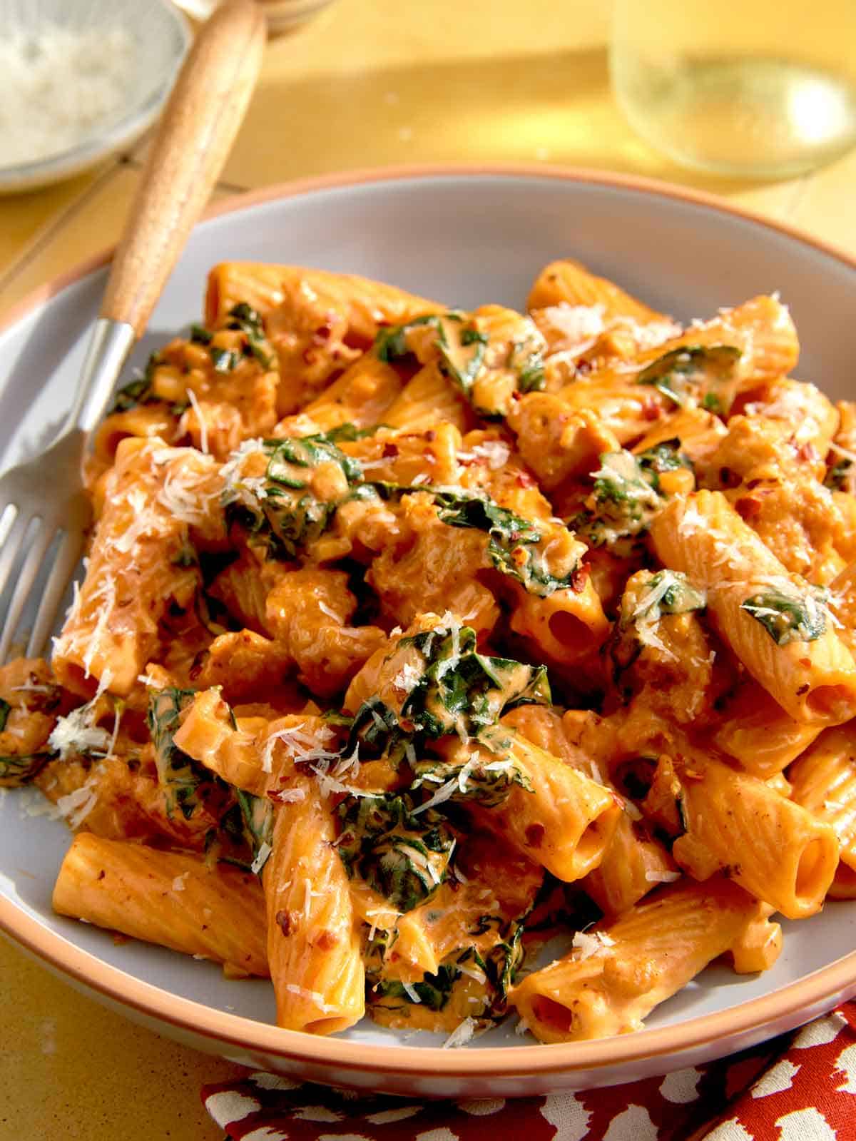 A bowl of kale and sausage rigatoni with a fork on the side.