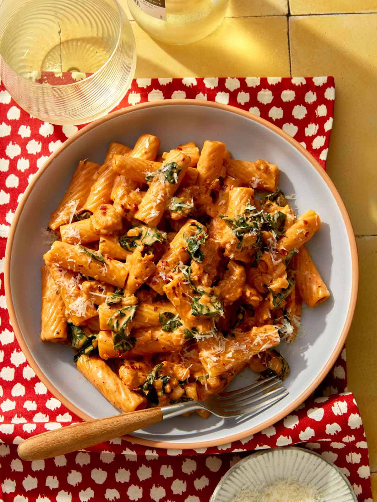 Kale and sausage rigatoni pasta in a bowl with wine on the side.