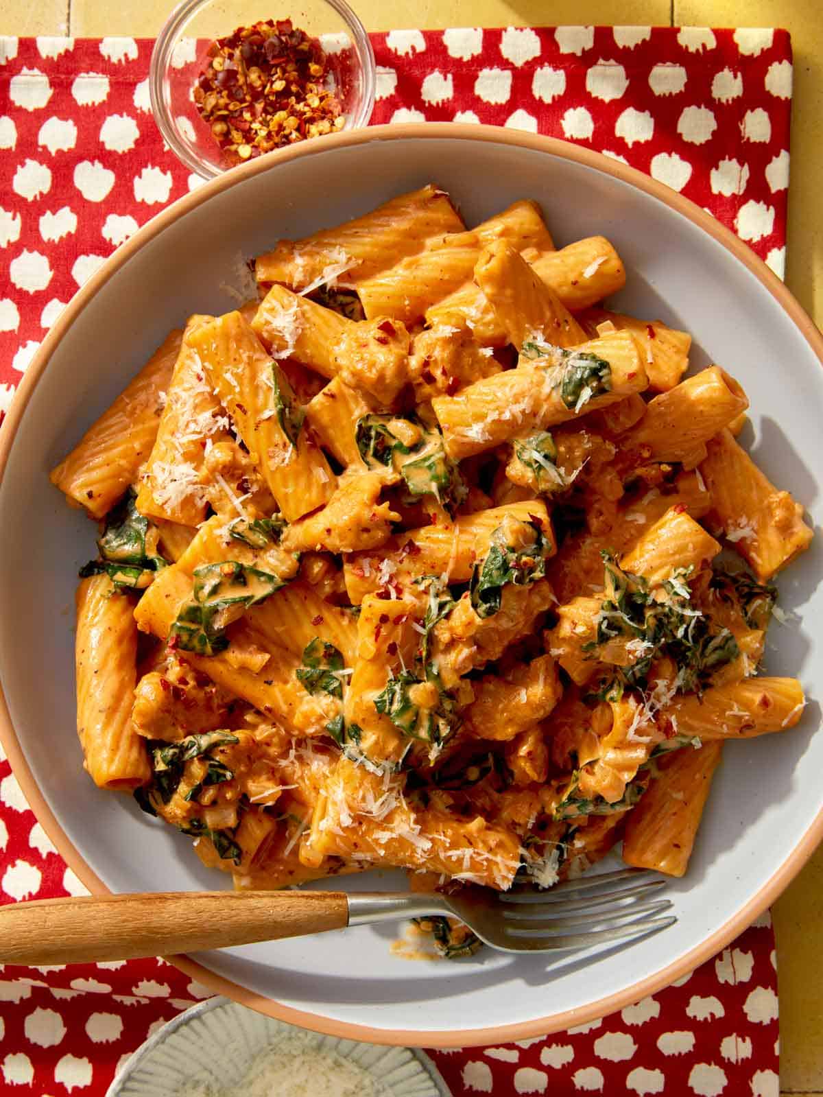 Close up on a bowl of kale and sausage rigatoni in a bowl with a fork. 