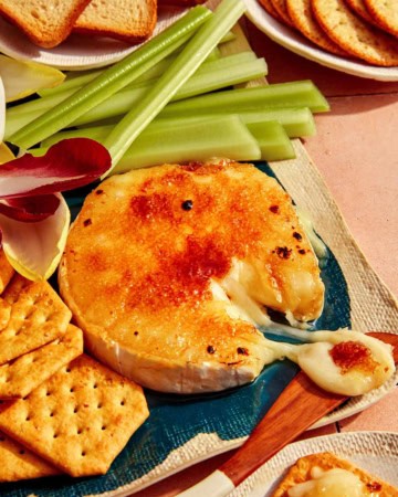 Honey Brûlée Brie on a platter with a knife taking some cheese.