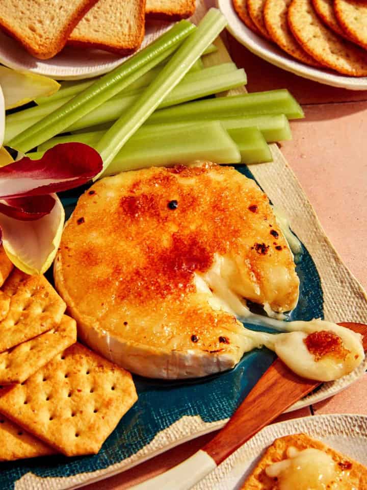 Honey Brûlée Brie on a platter with a knife taking some cheese.