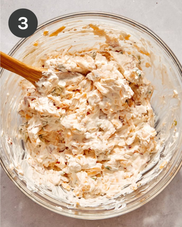 Million dollar dip mixed in a glass bowl with a wooden spoon.