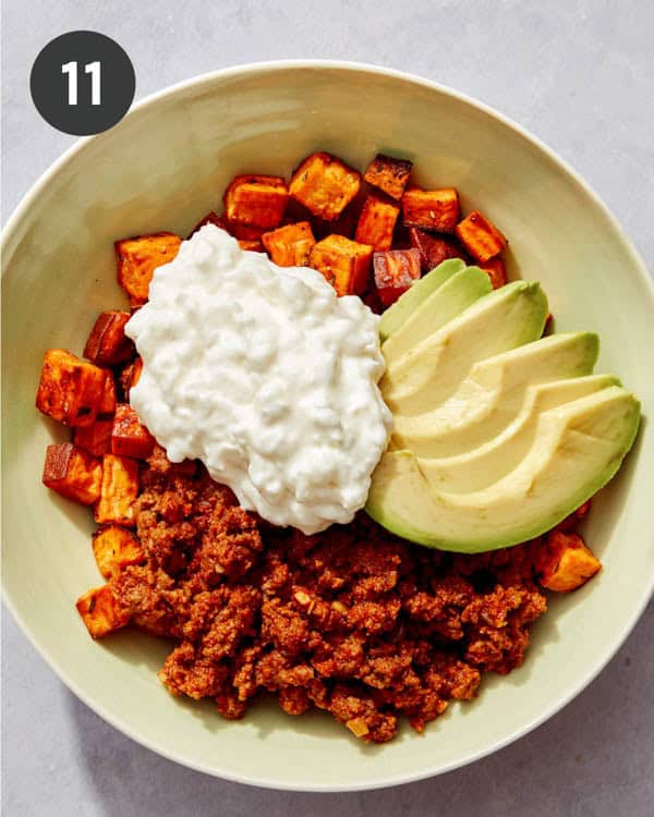 Roasted sweet potatoes and ground beef in a bowl with cottage cheese and avocado on top.