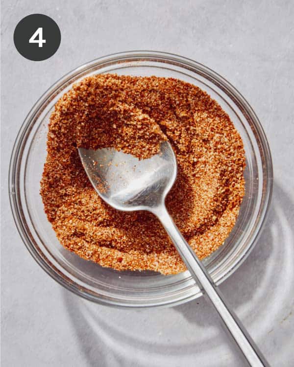 Taco seasoning mixed together in a glass bowl with a metal spoon.