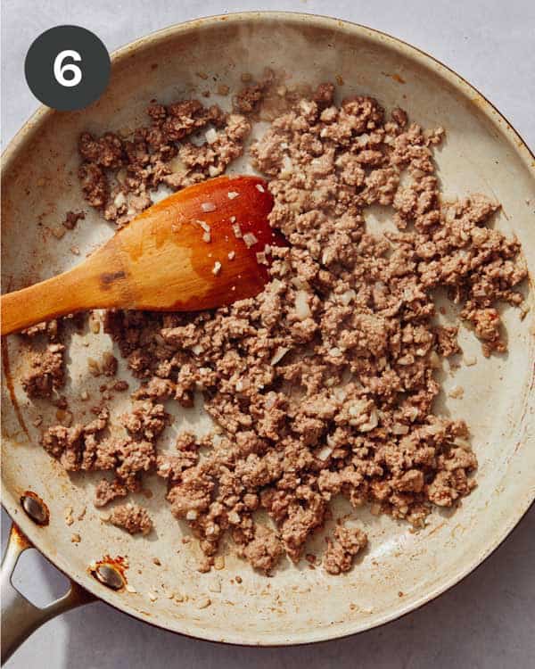Ground beef being cooking in a skillet with wooden spoon.