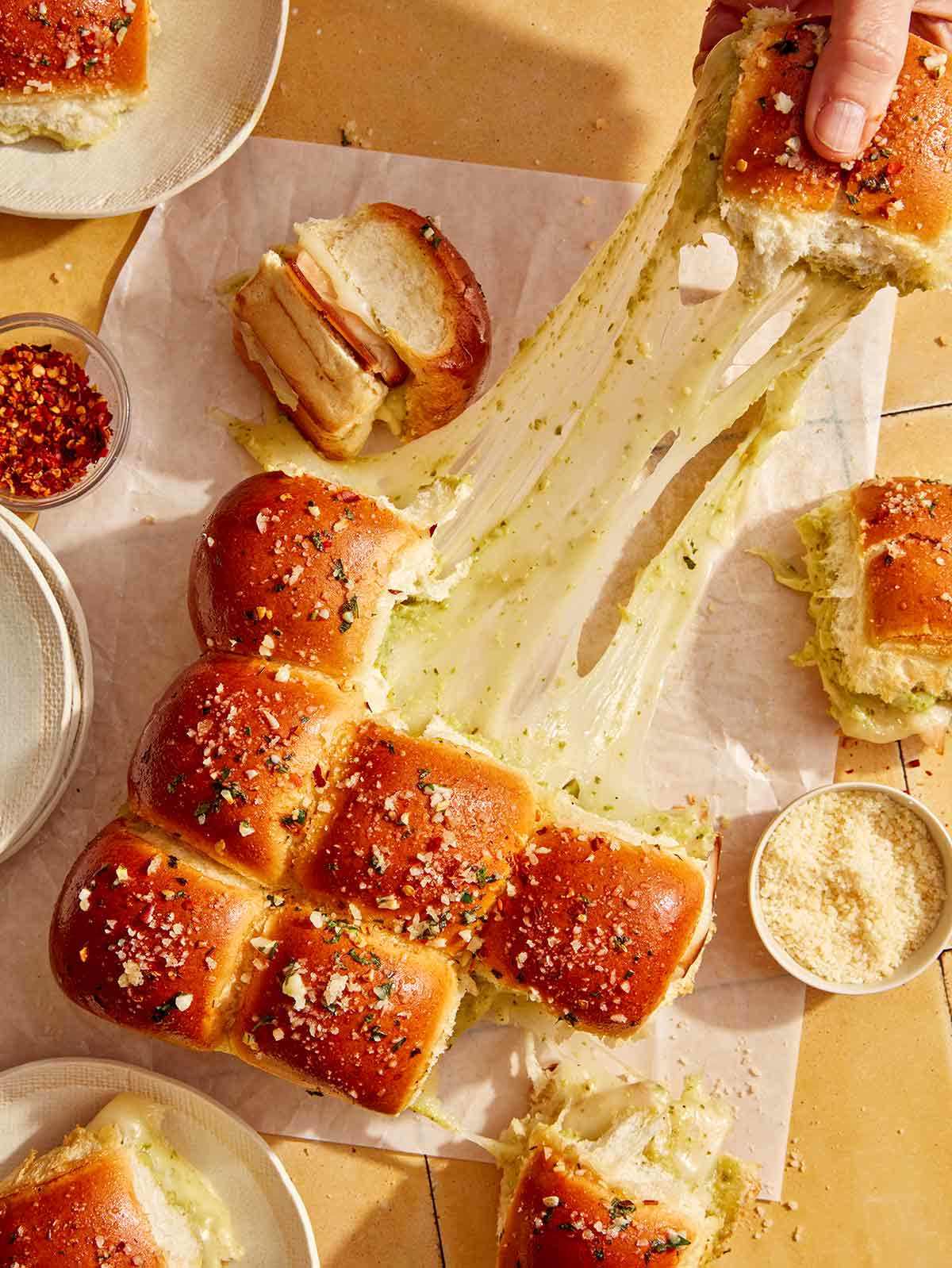 Hawaiian rolls made into a pesto and turkey sandwich being pulled apart with gooey cheese.