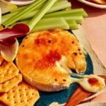 Honey Brûlée Brie on a platter with a knife taking some cheese.