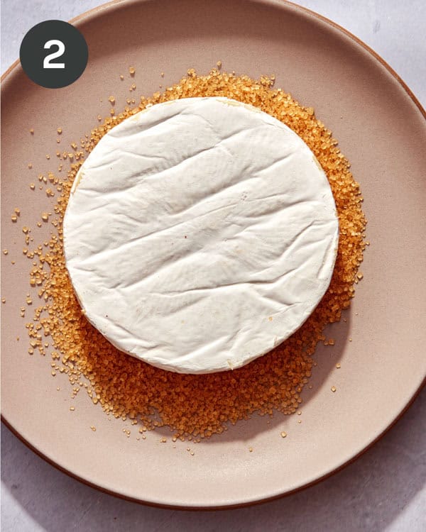 A wheel of brie being pressed into sugar.