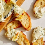 Baked garlic bread dip on crostini for an appetizer.