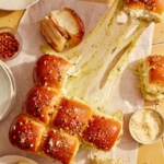 Hawaiian rolls made into a pesto and turkey sandwich being pulled apart with gooey cheese.