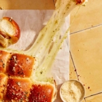 A hand grabbing a slider from a piece parchment with a big cheese pull.