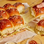 Hawaiian roll sliders being grabbed with a hand and showing a cheese pull.