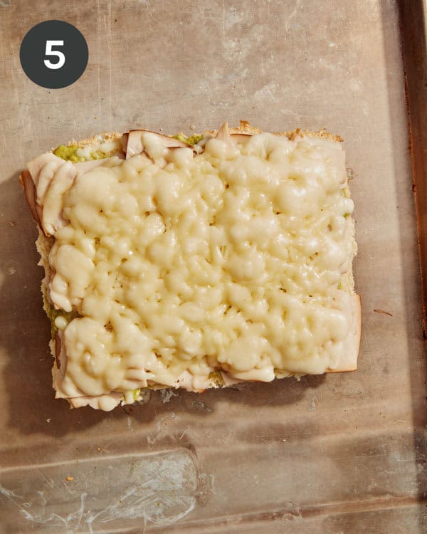 Melted cheese on a half of a sheet of hawaiian rolls.