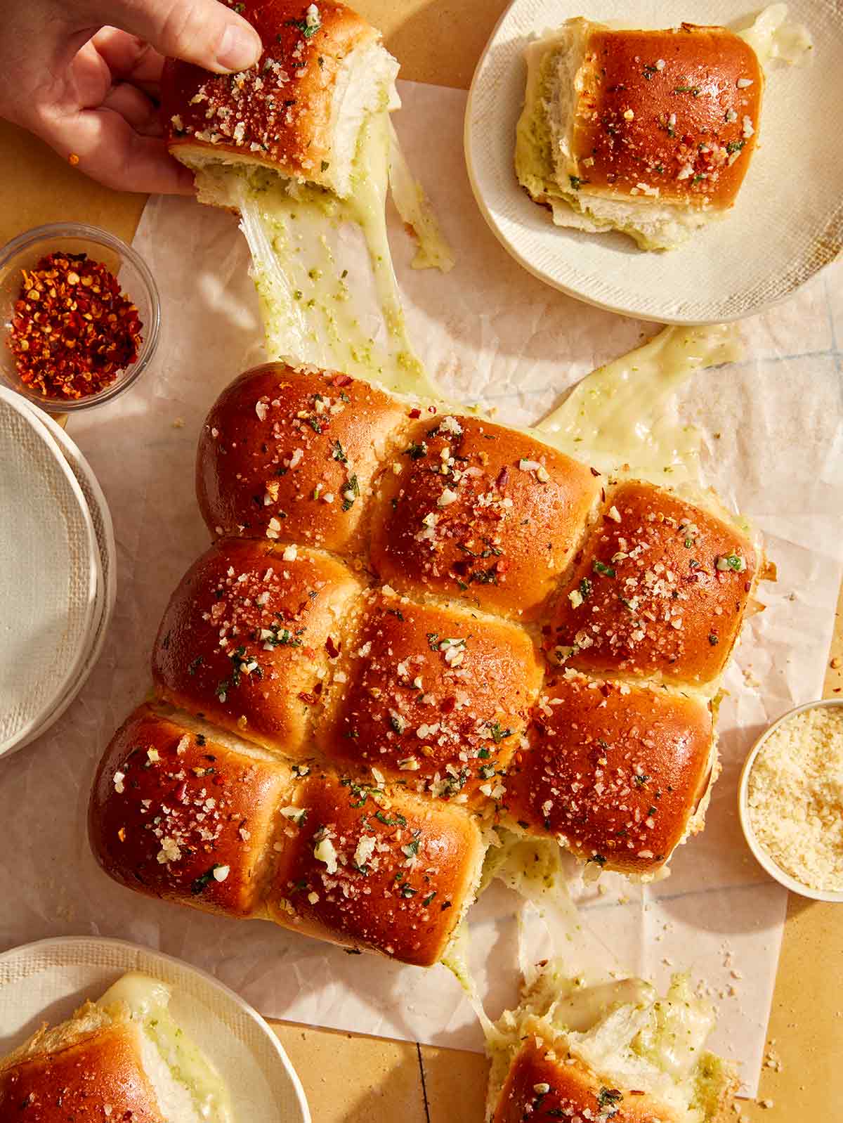 Hawaiian rolls made into a pesto and turkey sandwich being pulled apart with gooey cheese.