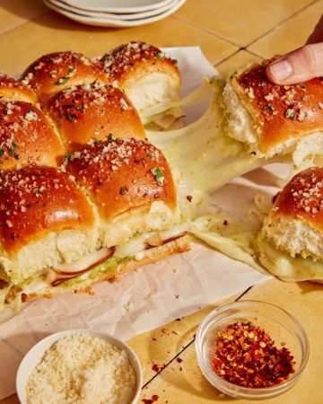 Hawaiian roll sliders being grabbed with a hand and showing a cheese pull.