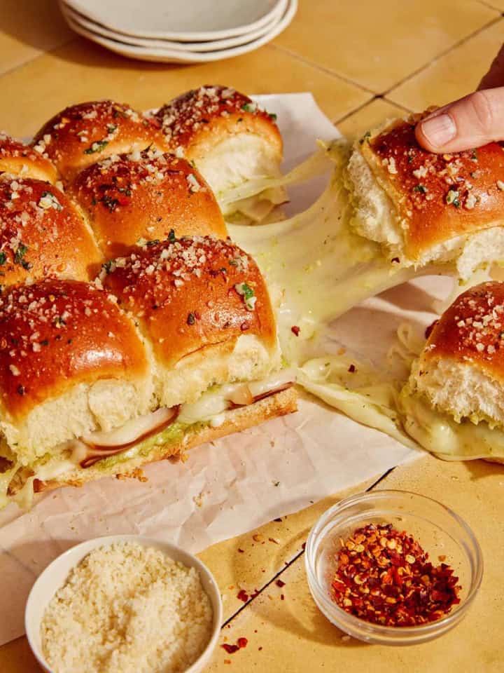 Hawaiian roll sliders being grabbed with a hand and showing a cheese pull.