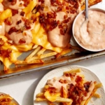 Animal style fries on a baking sheet served on plates.
