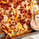 Animal style fries on a baking sheet with dressing on the side.