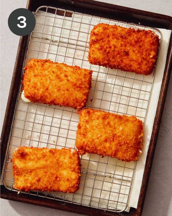 Freshly fried mozzarella sticks on a baking sheet.