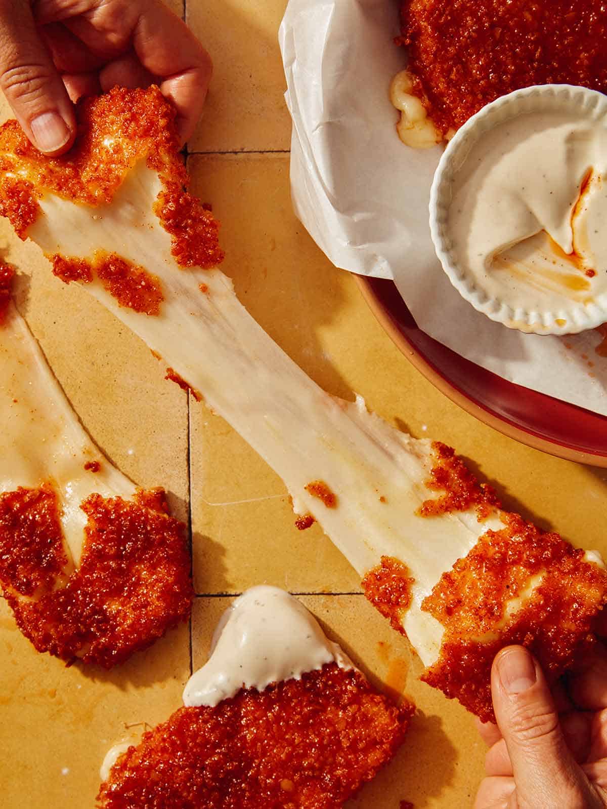 A big cheese pull from a mozzarella stick with hands pulling it apart.