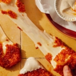 A big cheese pull from a mozzarella stick with hands pulling it apart.