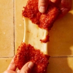 Someone ripping apart a mozzarella stick with a cheese pull being shown.