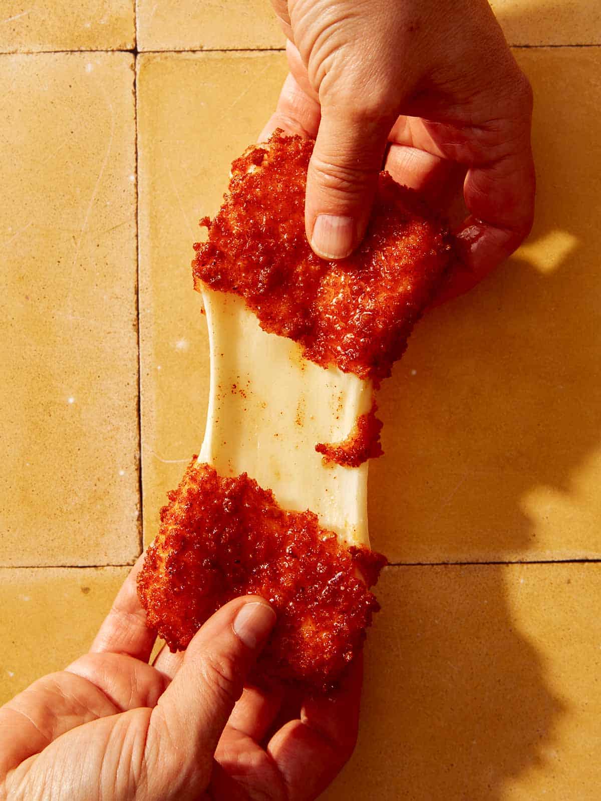 Someone ripping apart a mozzarella stick with a cheese pull being shown.