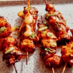 Air fryer bang bang chicken skewers on a platter with sauce being poured on top.