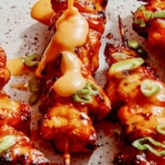 Air fryer bang bang chicken skewers on a platter with sauce being poured on top.