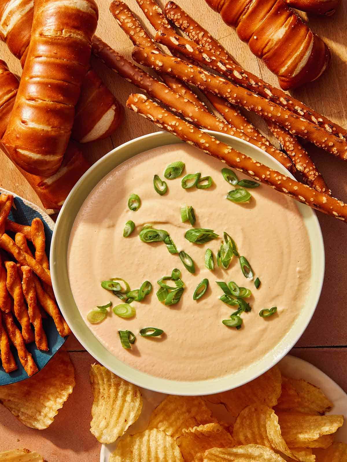 Crock pot beer cheese dip in a bowl being served with pretzels and chips.