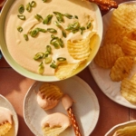 Crock pot beer cheese dip in a bowl with bread and chips all around it.