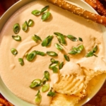 Crock pot beer cheese dip in a bowl with bread and chips all around it.