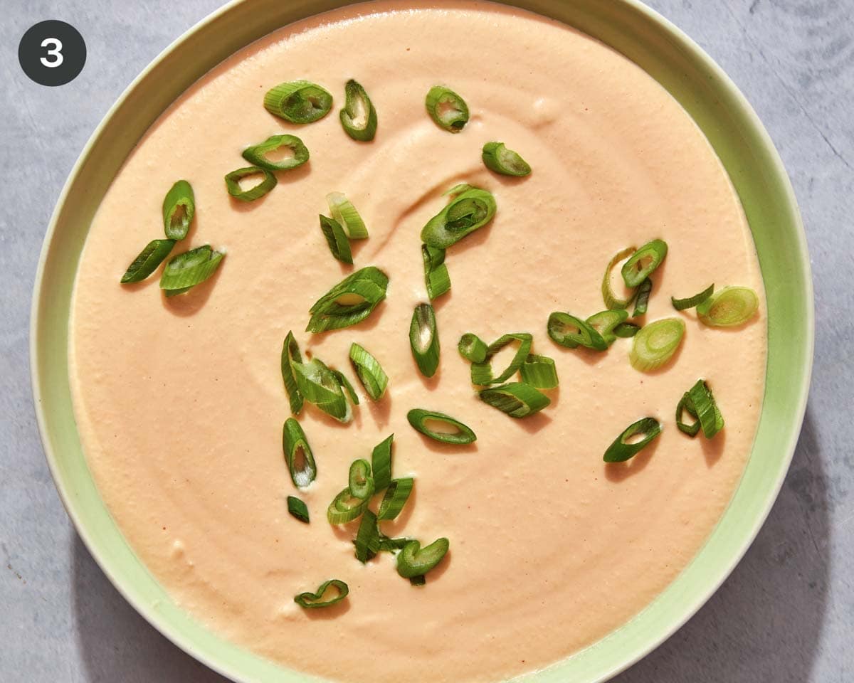 A bowl of crock pot beer cheese dip with green onions on top.