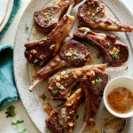 Garlic butter lamb chops recipe on a platter with plates next to it.
