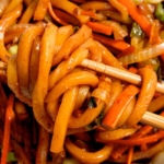 Yaki udon noodles with chop sticks taking a bite.