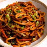Udon noodles in a bowl with green onions on top.