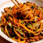 Yaki udon noodles with chop sticks taking a bite.