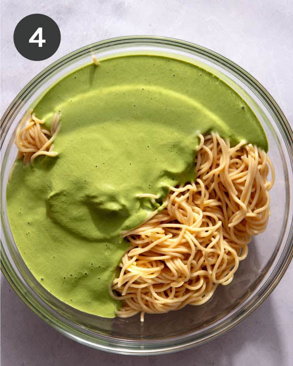 A glass bowl with cooked spaghetti in it and a green sauce poured over top.